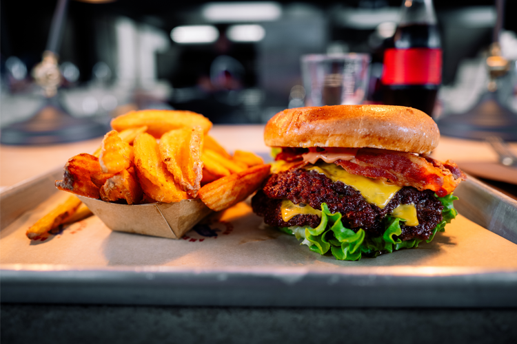 Saftig hamburger med bacon og cheddarost, servert med søtpotetfries på en metallplate.