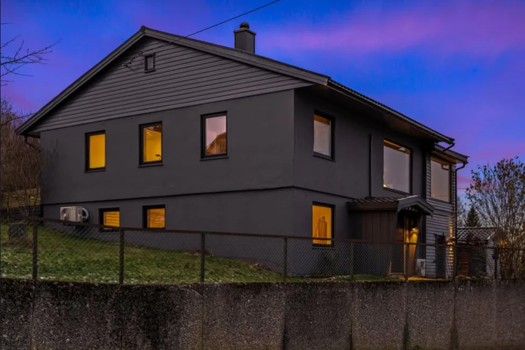 Moderne, grått hus med store vinduer og en hage, beliggende i et rolig nabolag under en fargerik himmel.