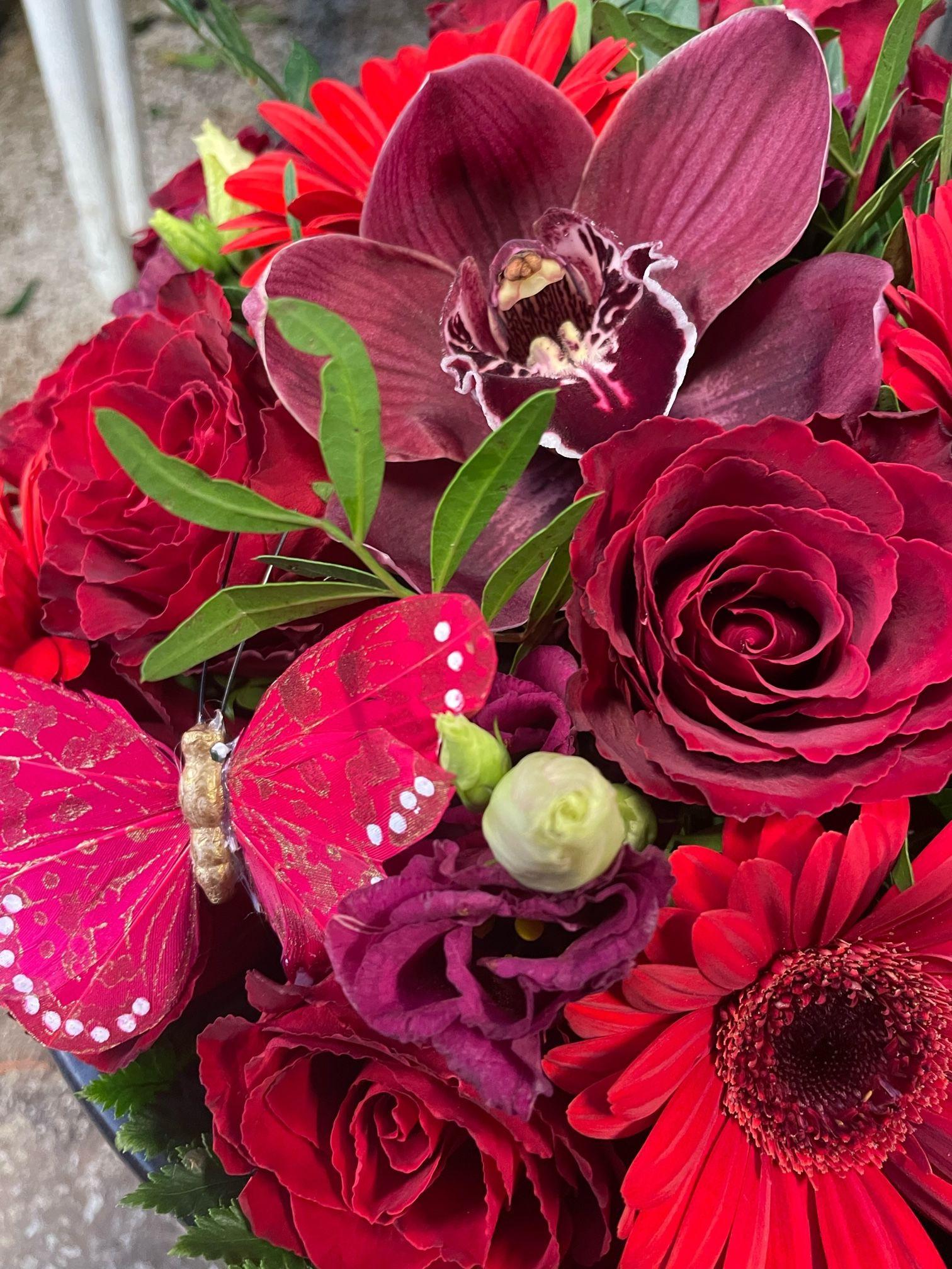 En bukett med røde blomster, inkludert roser, gerbera og orkideer, med en rosa sommerfugl som sitter på blomstene.