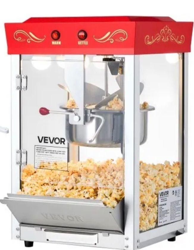 Popcornmaskin med rød topp, glassdører og en stor kjele fylt med fersk popcorn.