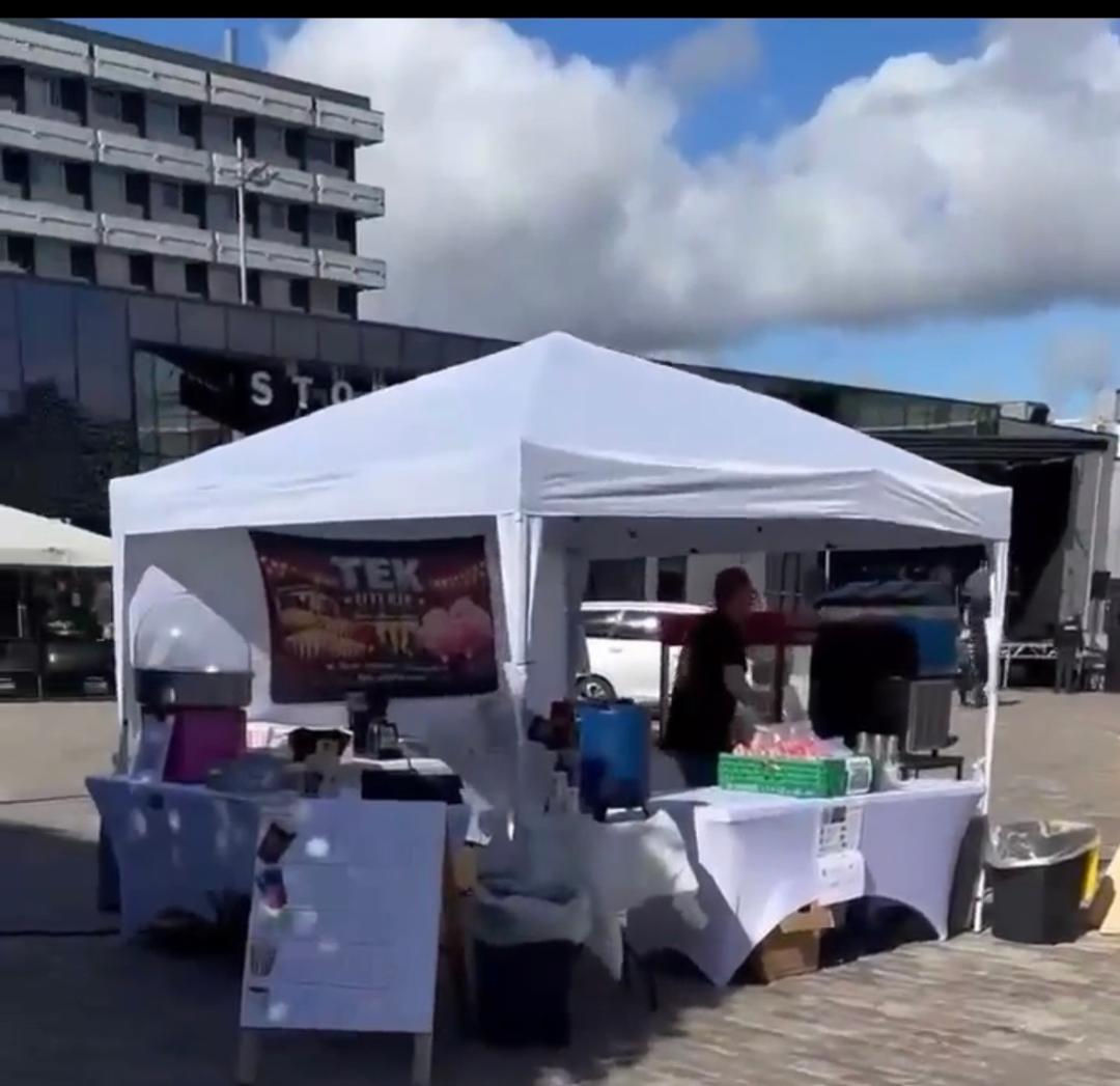 Telt med mat- og drikkesalg på en utendørs festival, med bygninger og blå himmel i bakgrunnen.