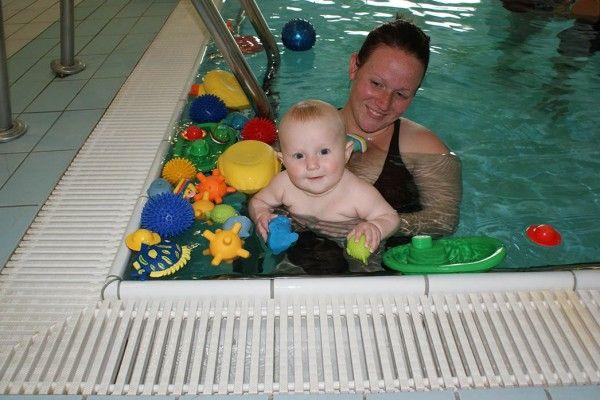 Mor og baby leker i svømmebassenget med fargerike leker rundt dem.