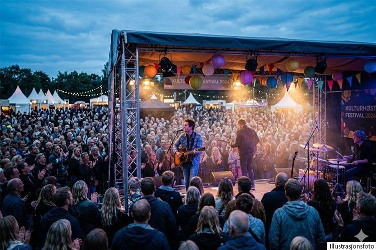 En stor folkemengde ser på en konsert på en festival med fargerike ballonger og lys i bakgrunnen.