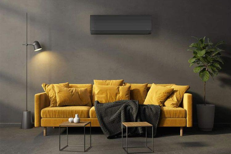 Moderne stue med en gul sofa, puter, et svart teppe og små bord, samt en plante og en lampe.