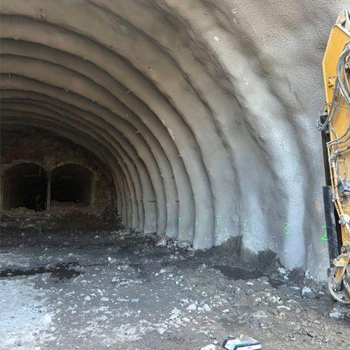 Innvendig av en tunnel med buede vegger og grus på bakken, med en maskin synlig til høyre.