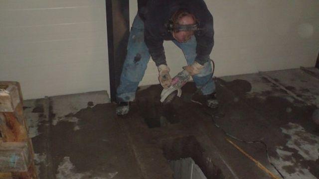 En person som bruker en elektrisk verktøy for å kutte i betonggulvet i et rom.