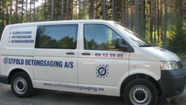 En varebil fra Østfold Betongsaging A/S parkert i skogen, med logo og kontaktinformasjon synlig på siden.