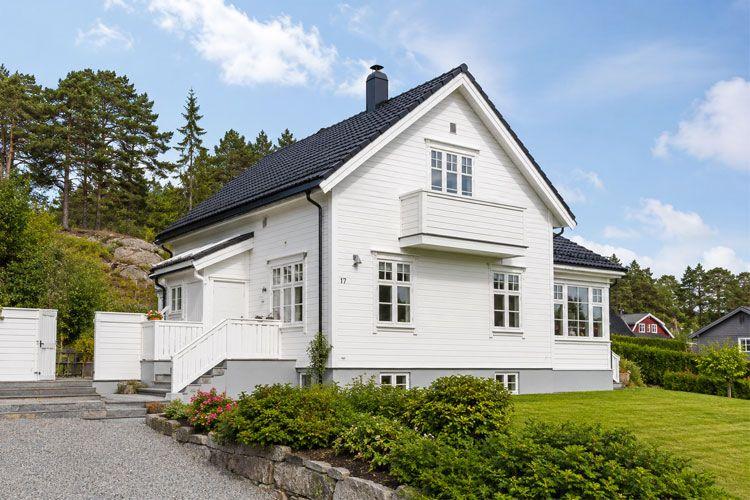 Moderne, hvit enebolig med balkong og hage, omgitt av trær og grøntområde.