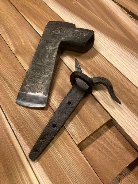 To verktøy laget av metall, en øks og en spiker, ligger på et bord av ubehandlet tre.