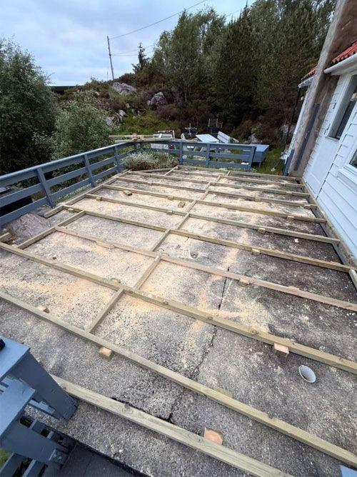 Bilde av en terrasse med trestammer og sagflis, klar for oppussing og legging av nytt gulv.