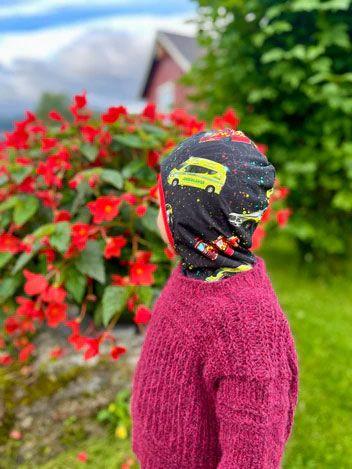 Barn med fargerik lue står foran blomstrende røde planter i hagen.