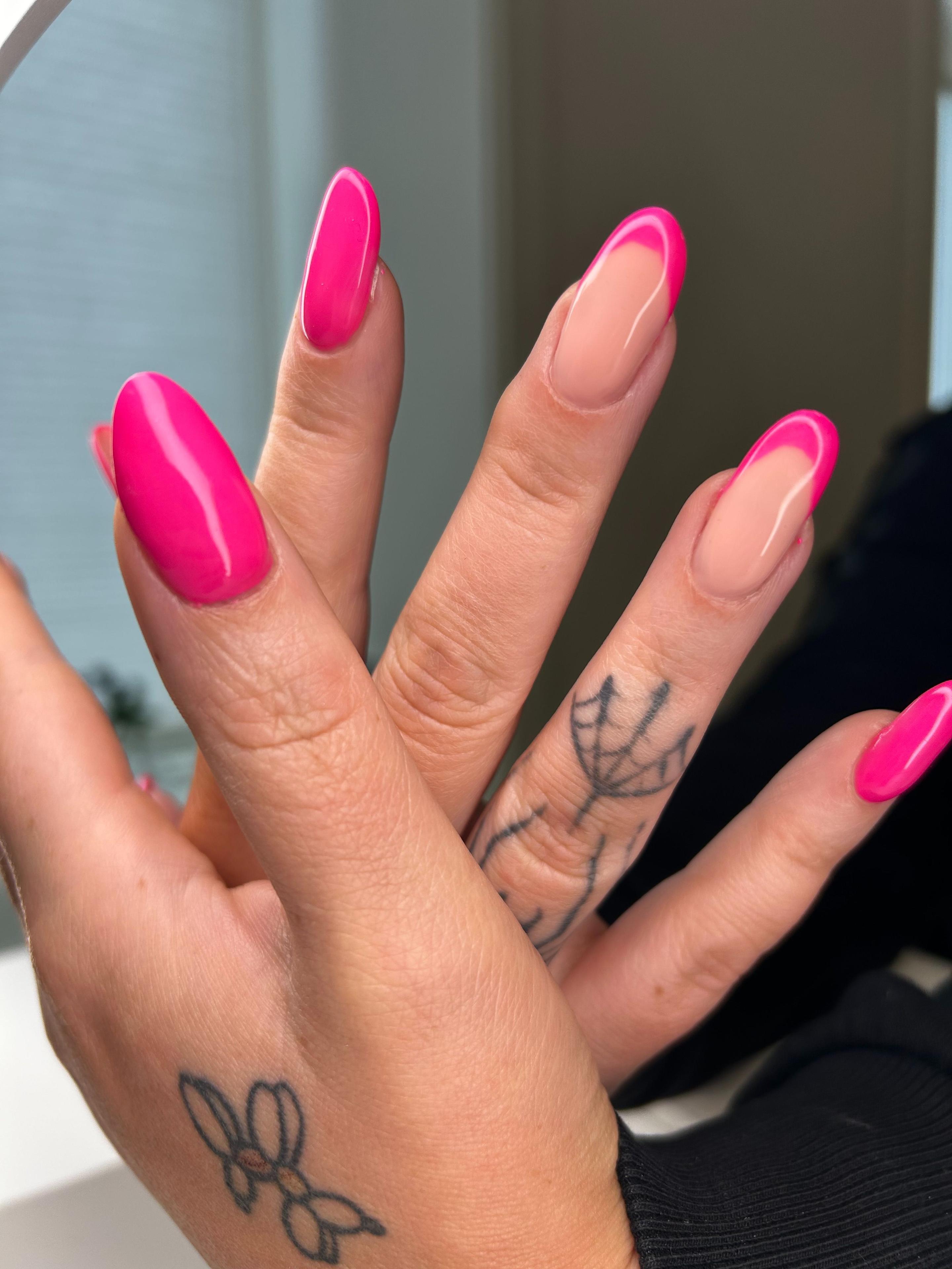 Hender med lange, rosa negler og tatoveringer på håndleddene, med en naturlig neglebase.