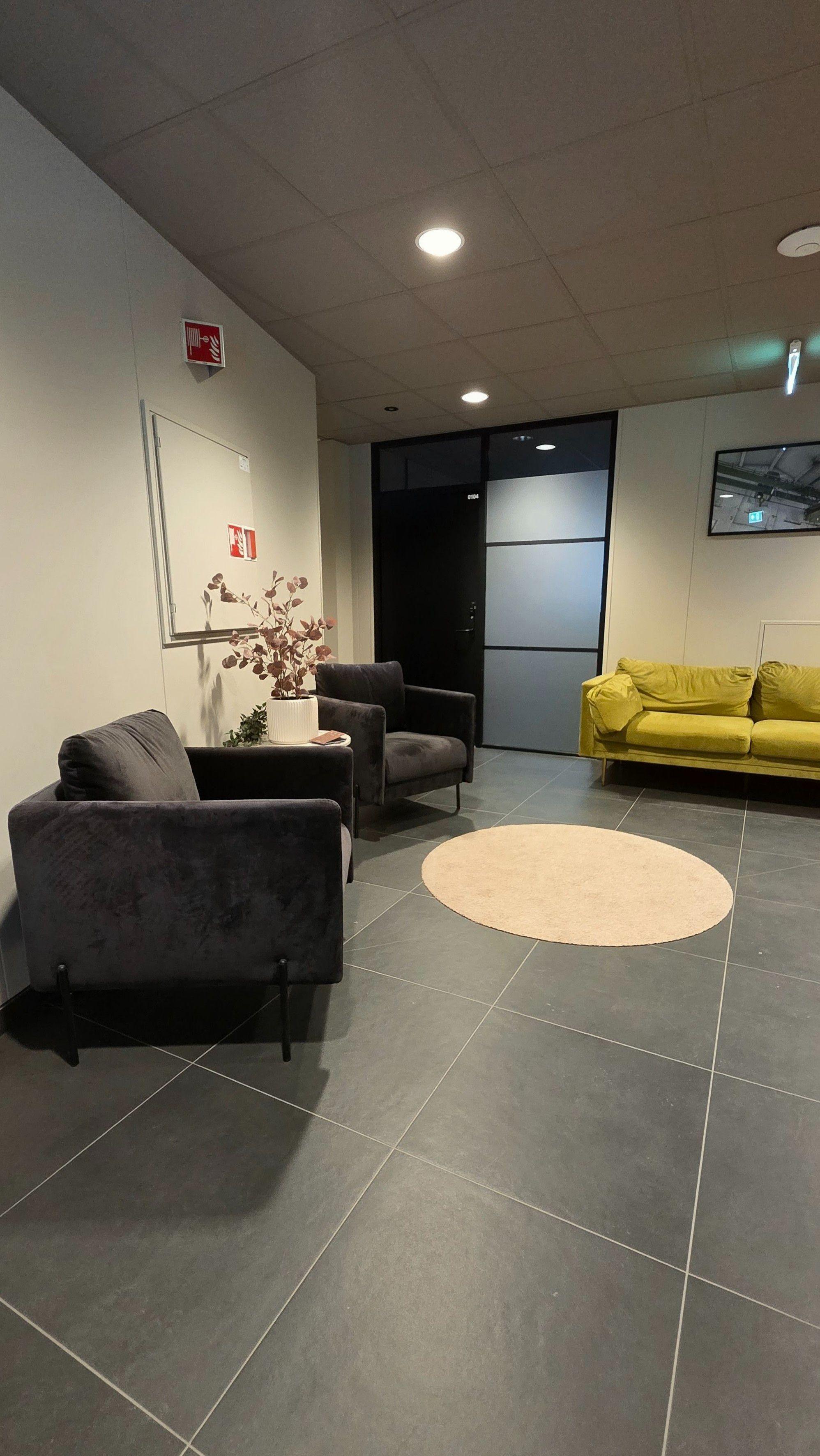 Moderne inngangsparti med grå stoler, en grønn sofa og en rund matte på flislagt gulv.