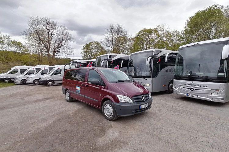 En rød minibuss står foran flere grå og sølvfargede busser på en parkeringsplass.