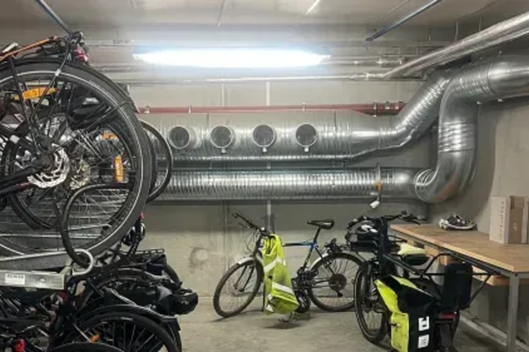 Sykkelparkering i kjeller med flere sykler og ventilasjonsrør på veggen.