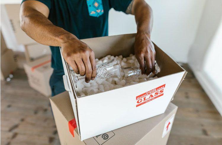 En person pakker inn glassvarer i en eske med bobleplast og fyllmateriale.