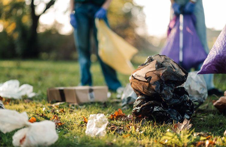Personer plukker opp søppel i en park, med plastposer og pappesker spredt over gresset.