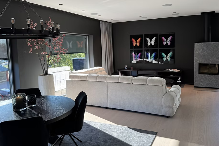 Moderne stue med lys sofa, svart spisebord, og fargerike sommerfugler på veggen. Store vinduer gir naturlig lys.