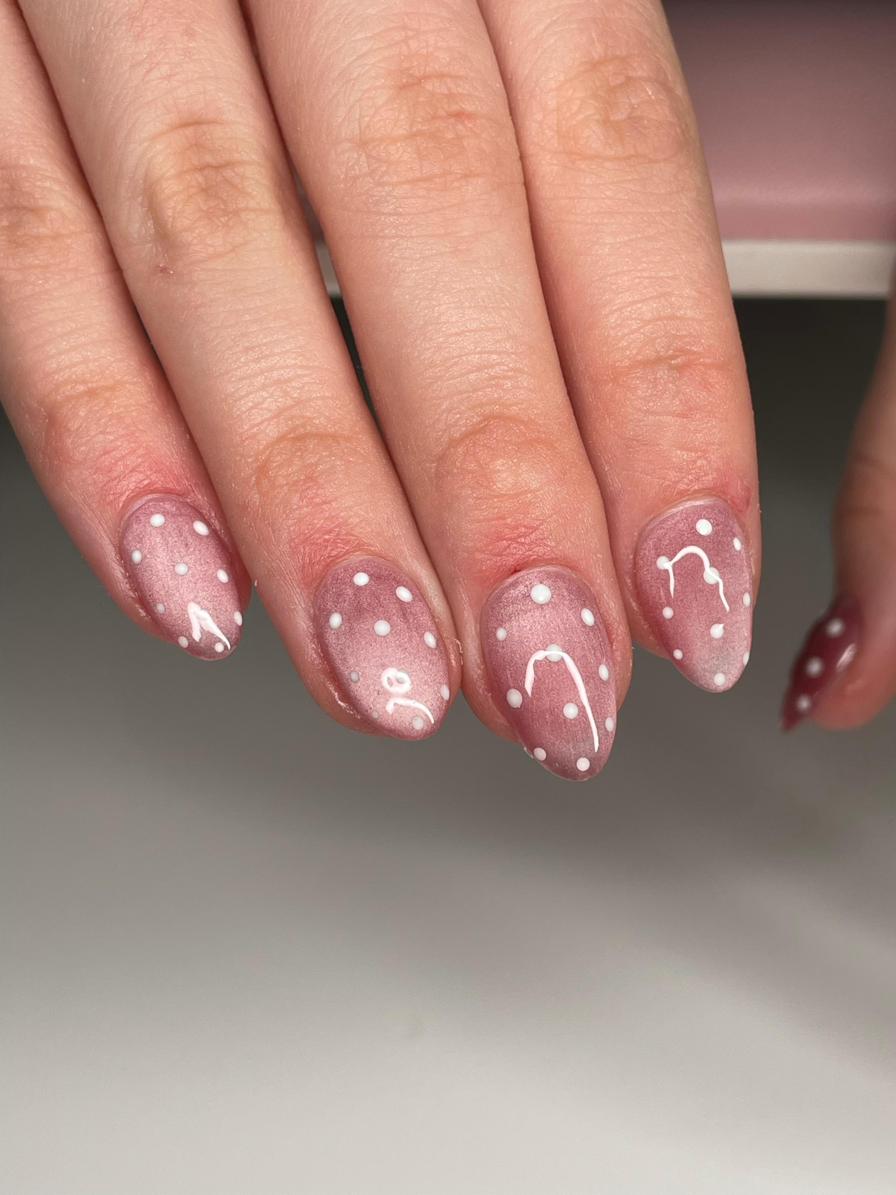 Hånd med rosa negler dekorert med hvite prikker og linjer, perfekt for en moderne negledesign.