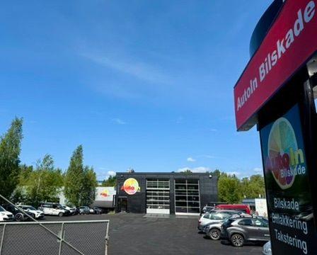 Bilde av Autolin Bilskade med moderne bygning, parkerte biler og klar blå himmel i bakgrunnen.