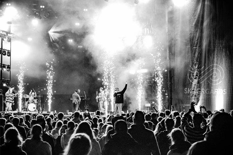 En konsert med band på scenen, lys og fyrverkeri, og et stort publikum som nyter musikken.