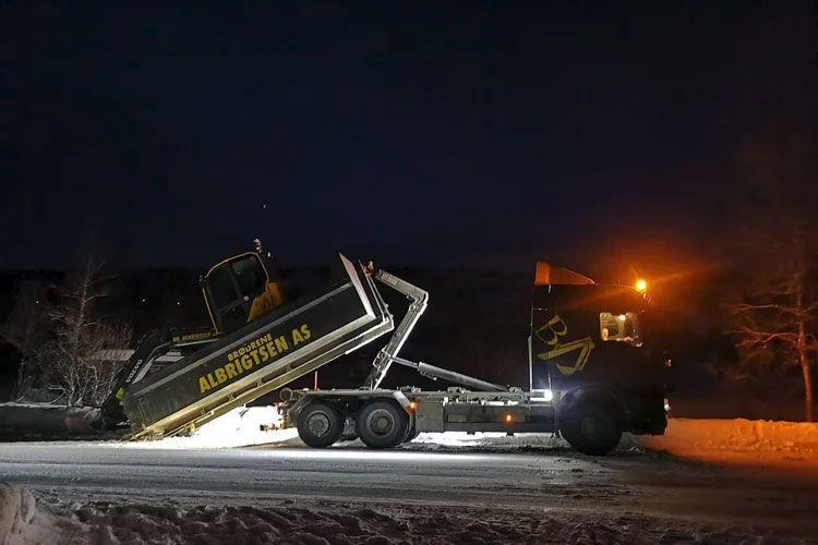 En snøplogbil i aksjon om natten, med lys som lyser opp snødekket vei.