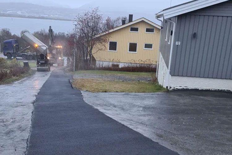 En lastebil med betongblander kjører opp en grå vei mot en gul bolig i regnvær.