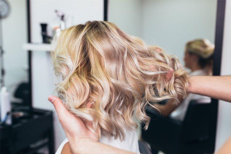 En frisør styler bølgete blondt hår i en salong, med fokus på hårets tekstur og bevegelse.
