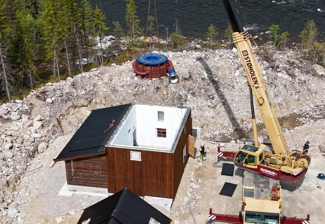 En byggeplass med en hytte, en kran og en oppblåsbar basseng i bakgrunnen ved en innsjø.