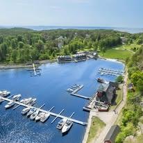 En vakker havn med flere båter, omkranset av grønn natur og blått vann under en klar himmel.