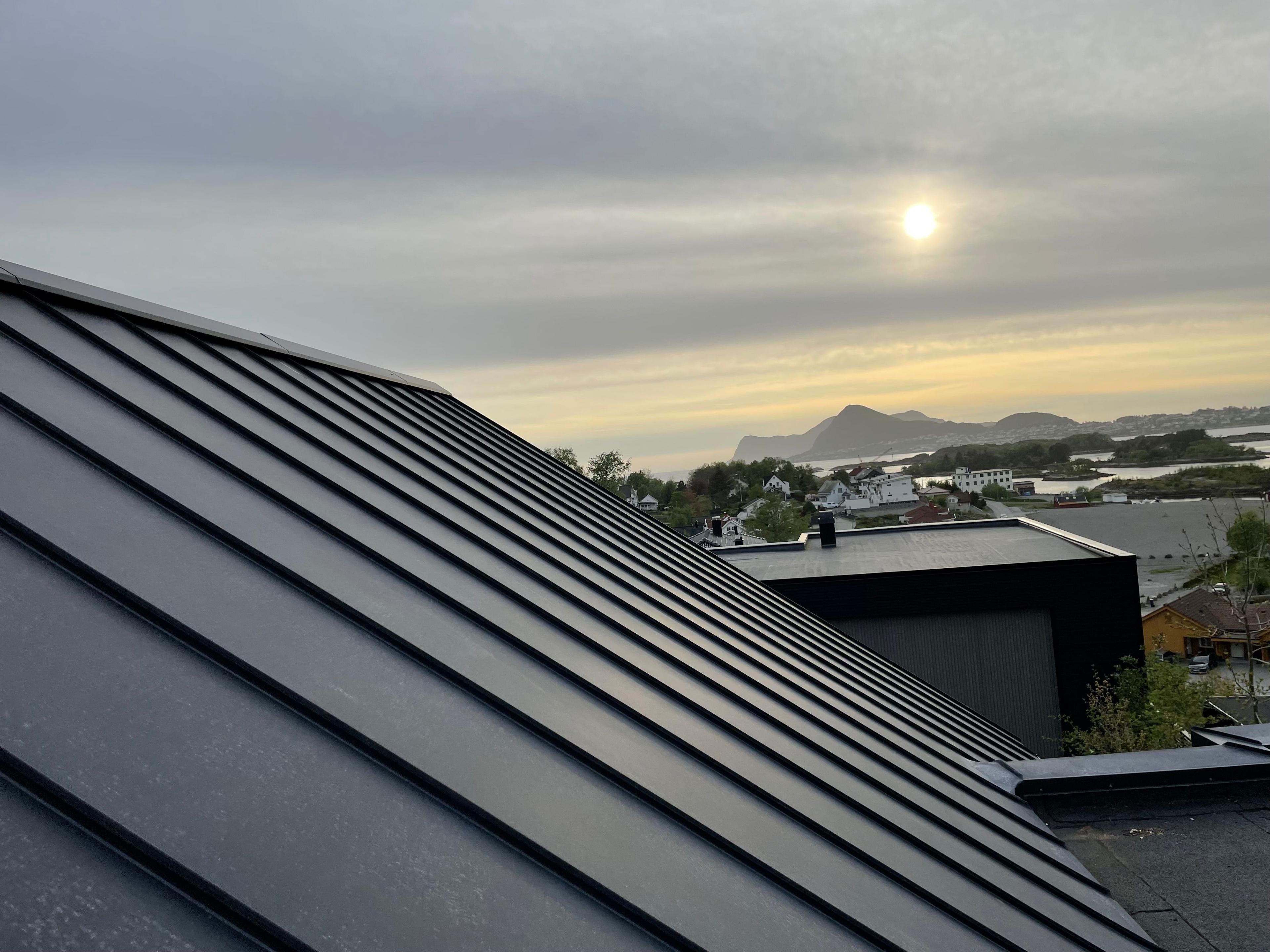 Tak med metallplater og solnedgang over fjorden og fjellene i bakgrunnen.