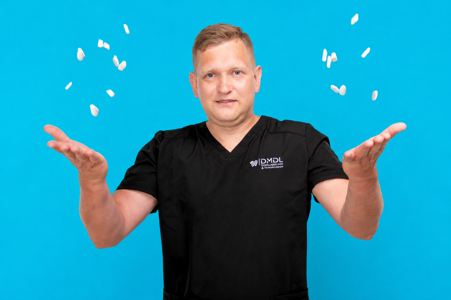 En mann i svart legeuniform som kaster små gjenstander opp i luften mot en blå bakgrunn.
