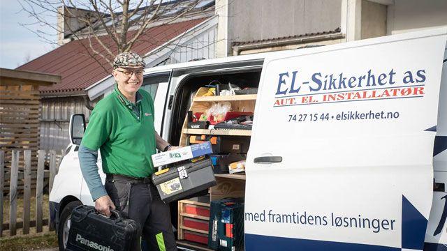 En smilende elektriker står ved en varebil fylt med verktøy og utstyr for elektriske installasjoner.