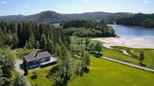 En vakker utsikt over et hus omgitt av trær, med en innsjø og fjell i bakgrunnen. Grønt gress dekker området.