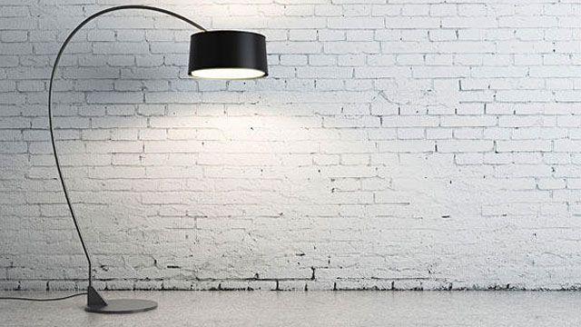 Moderne gulvlampe med buet arm og svart skjerm, plassert mot en hvit murvegg.