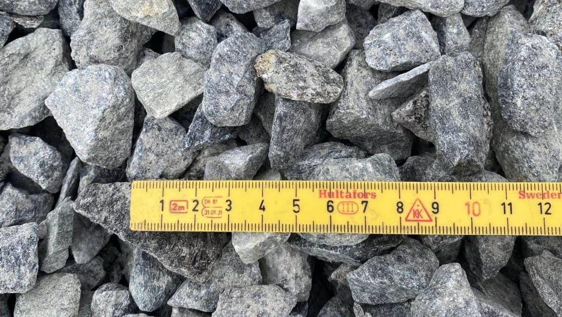 Grå steinmateriale med en målebånd som viser lengden på 20 centimeter, plassert på toppen av steinene.