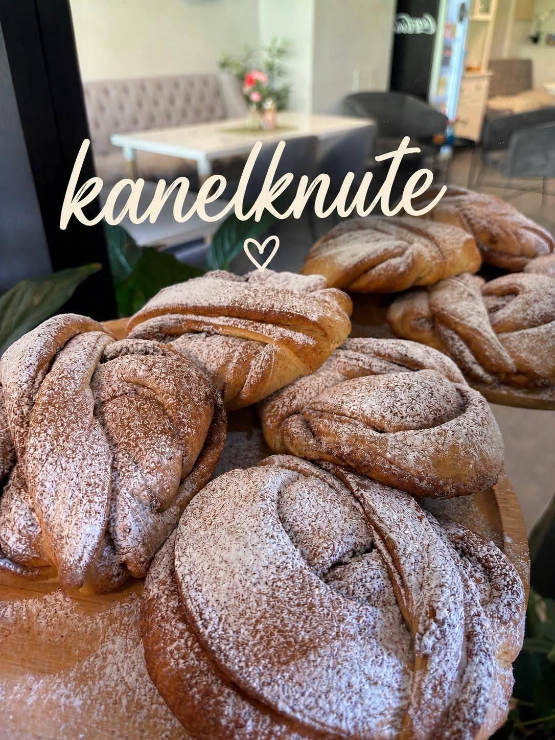Kanelknuter med melis på en treplate, plassert i et koselig kafémiljø.