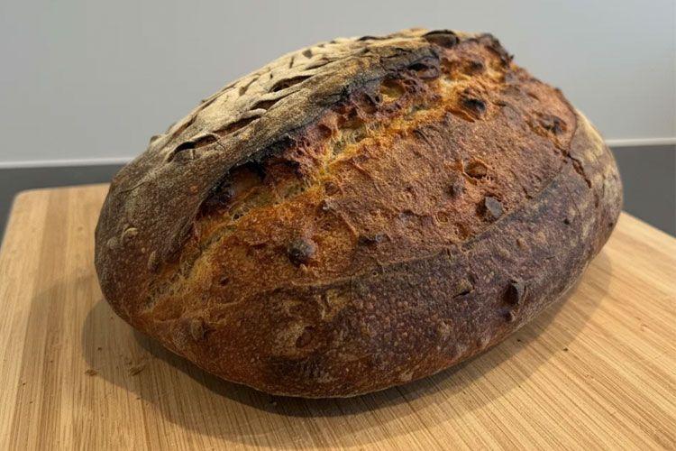 Et nybakt brød med sprø skorpe og gyllenbrun farge, plassert på en treplate.