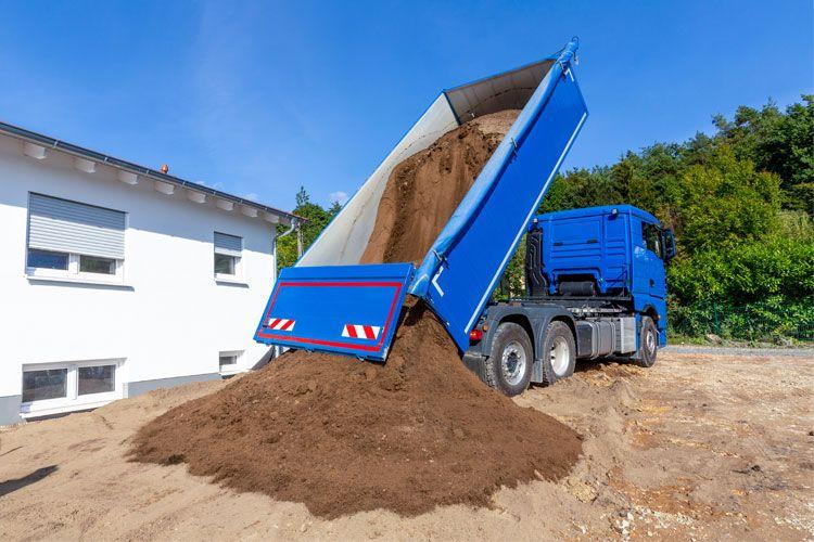 En lastebil som tømmer sand på en byggeplass under klar blå himmel.