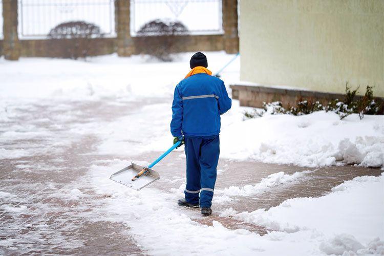 En mann i blå arbeidsklær som måker snø fra en oppkjørsel.