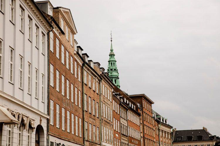 Fargerike bygninger med en grønn spir på toppen, som strekker seg langs en gate i København.