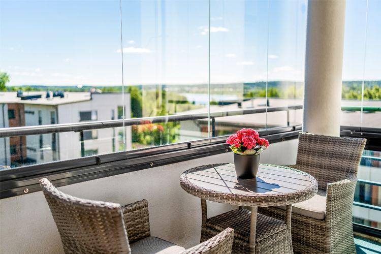 En balkong med utsikt, et bord med blomster og to stoler i flettet materiale.
