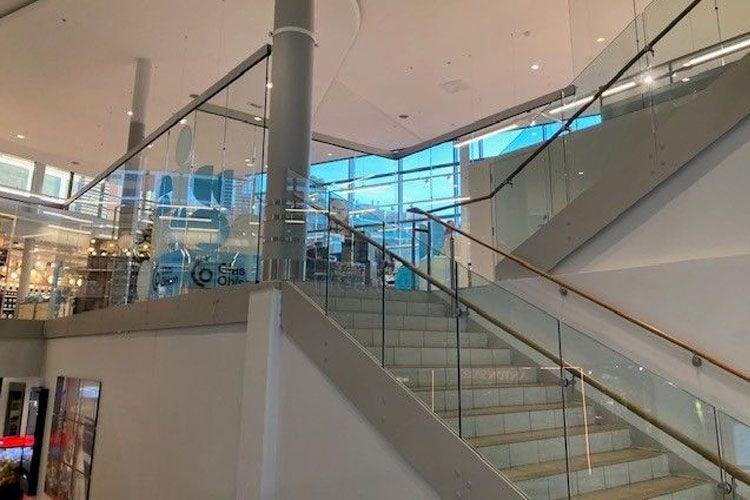 Moderne trapp med glassrekkverk i et kjøpesenter, med naturlig lys som strømmer inn gjennom vinduene.