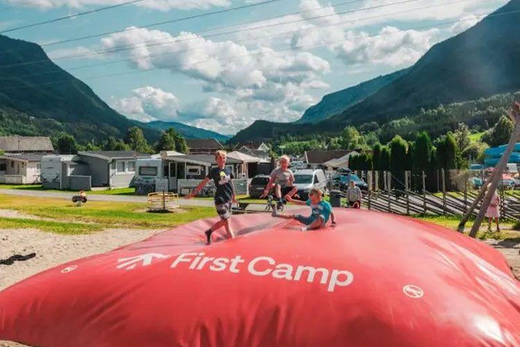 Barn hopper på en stor, rød luftpute i First Camp, med fjell og campingvogn i bakgrunnen.