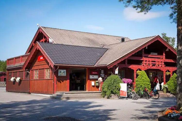 Rødt trehus med tak i skråning, blomsterkasser og sykler parkert foran inngangen.