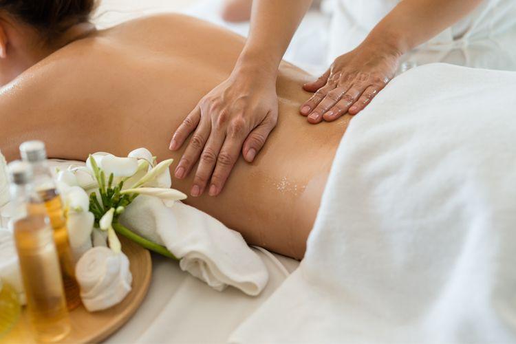 En person får massasje med olje, omgitt av velværeprodukter og blomster på et spa.
