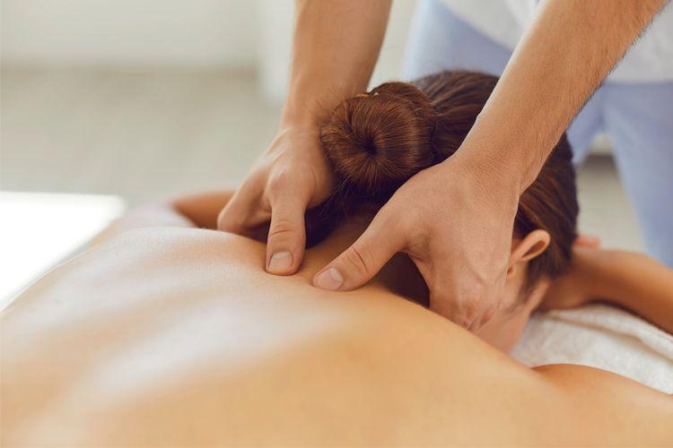 En person får massasje med fokus på ryggen i et lyst rom. Massasjehender jobber med musklene.