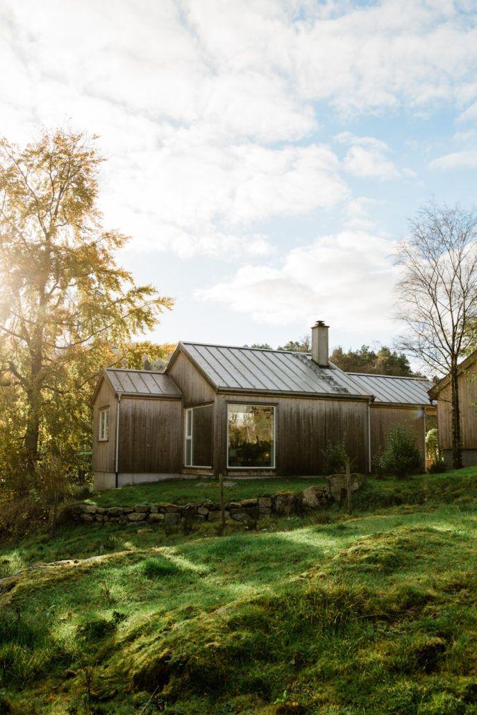 Moderne trehus med skråtak, omgitt av grønt gress og trær under en lys himmel.