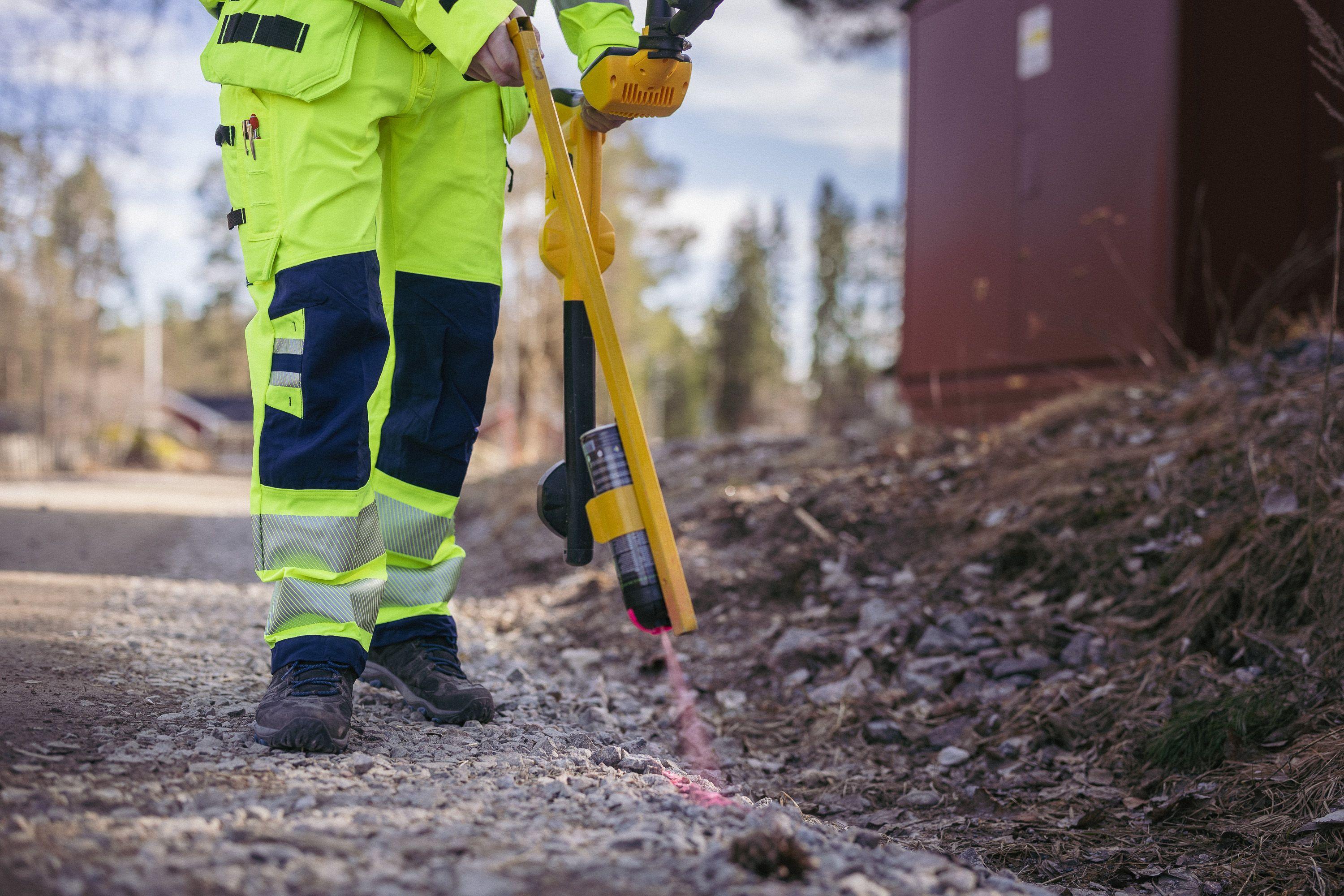 En person i refleksjakke bruker en kabelsøker på en grusvei i et skogsområde.