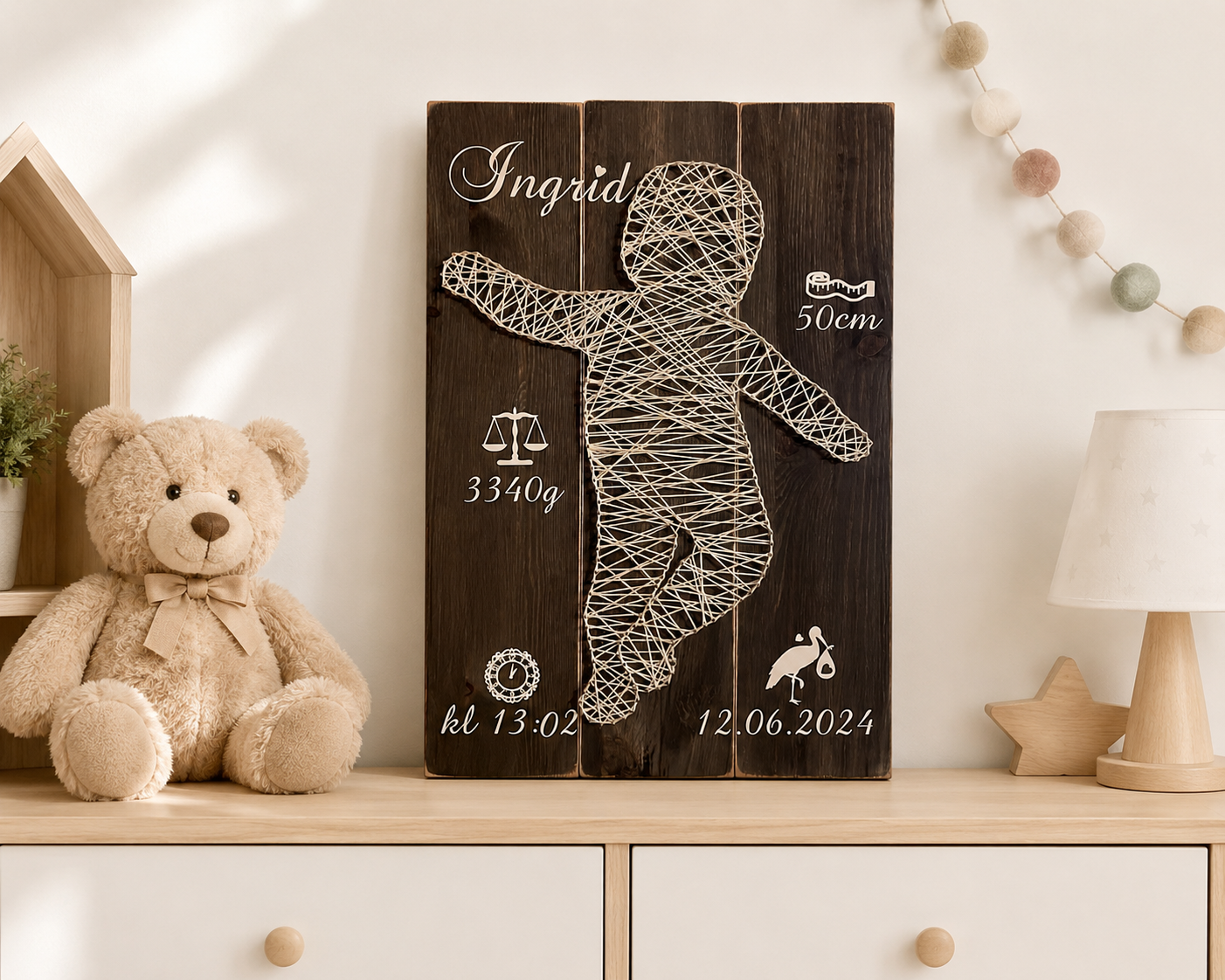 Bilde av en treplakat med navnet "Ingrid", fødselsinformasjon og en babyfigur, plassert på en hylle med en bamse.